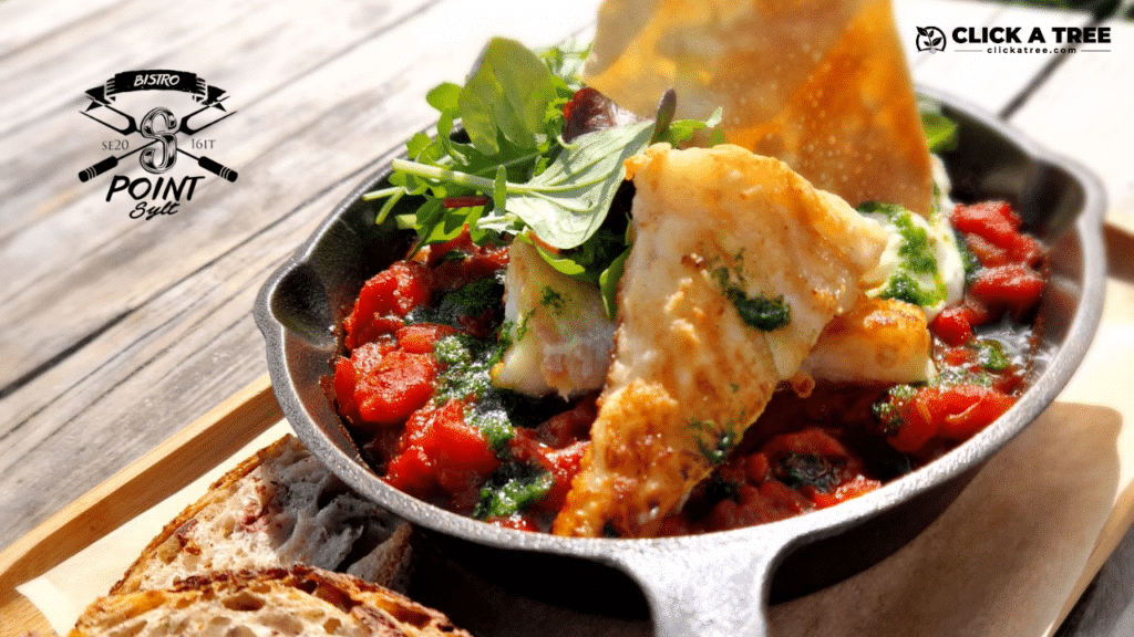 Shakshuka ein orientalisches Gericht mit frischem grünem Salat und einer Tomatensoße, serviert in einer kleinen gusseisernen Pfanne auf einem Holztisch im Bistro S-Point Sylt. Das Logo von S-Point Sylt und Click A Tree sind im Bild sichtbar, was das Engagement für Nachhaltigkeit hervorhebt